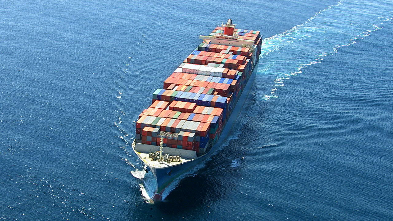 Containerschiff mit bunten Containern fährt über das blaue Wasser.