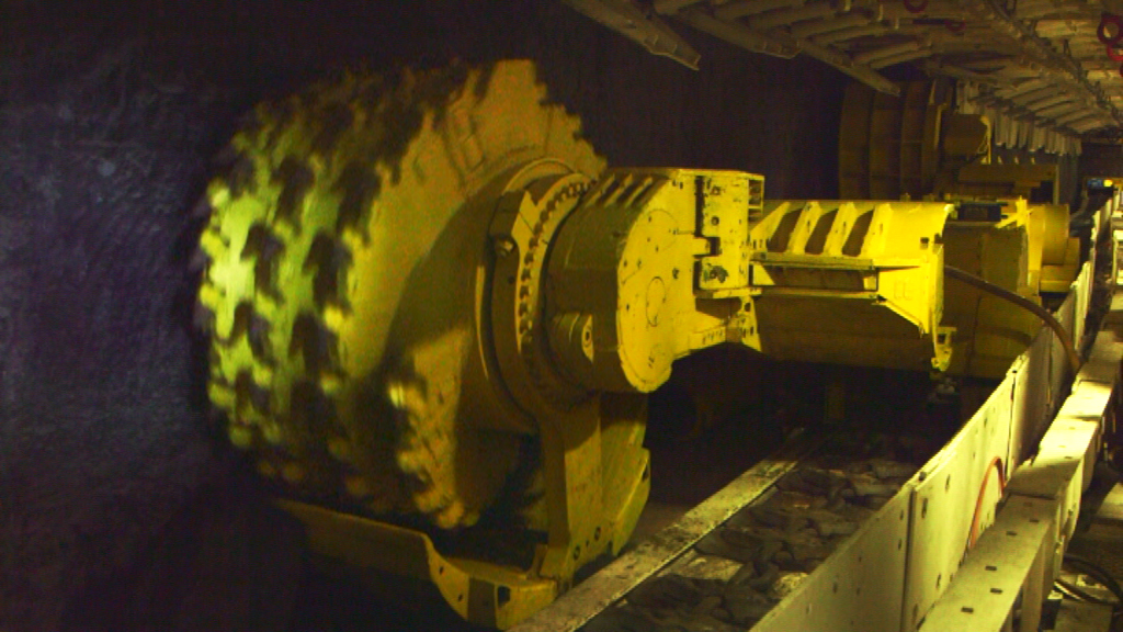 Großes gelbes Bergbaugerät mit rotierenden Zähnen, das Kohle aus einem Tunnel abbaut.