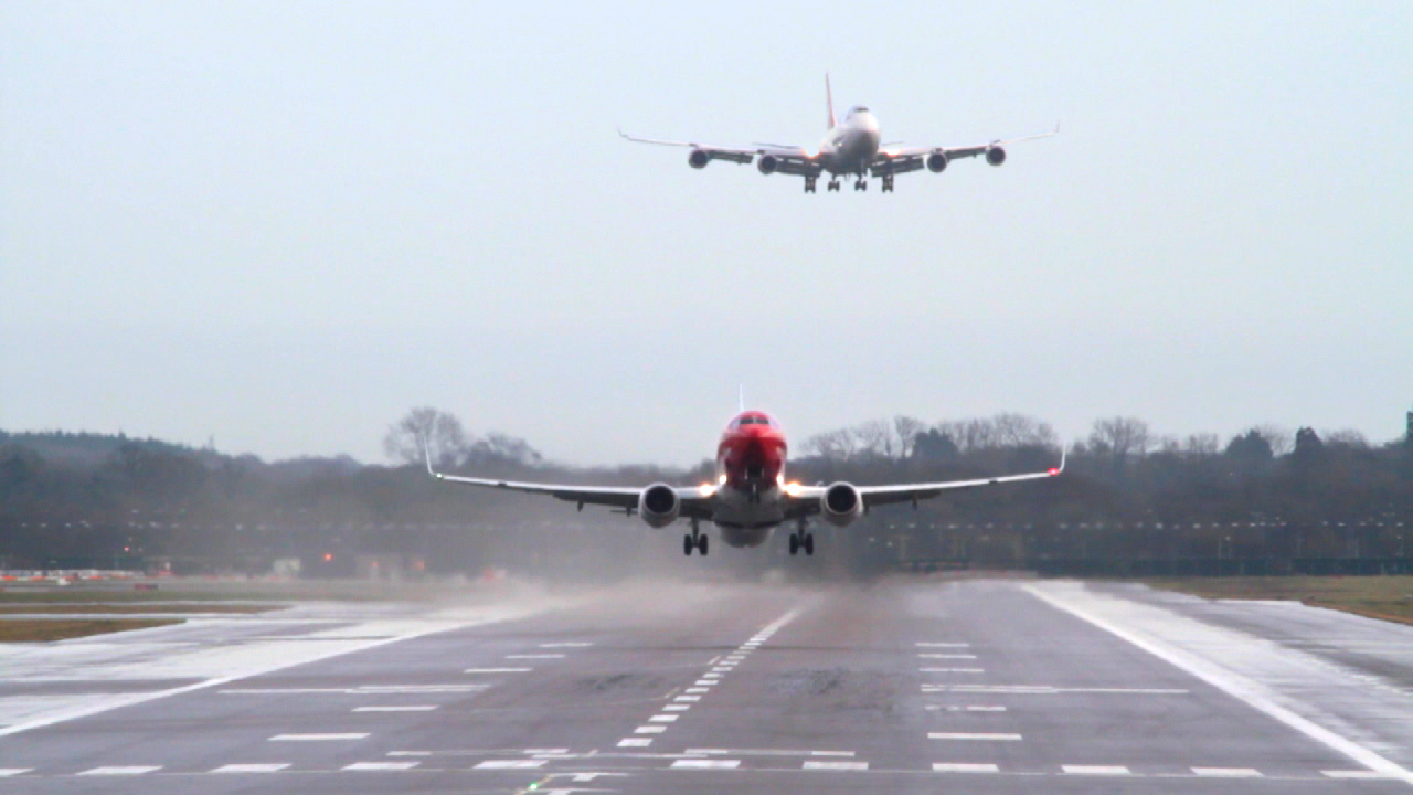 Ein Flugzeug landet auf einer Landebahn, während ein weiteres Flugzeug im Hintergrund im Anflug ist.
