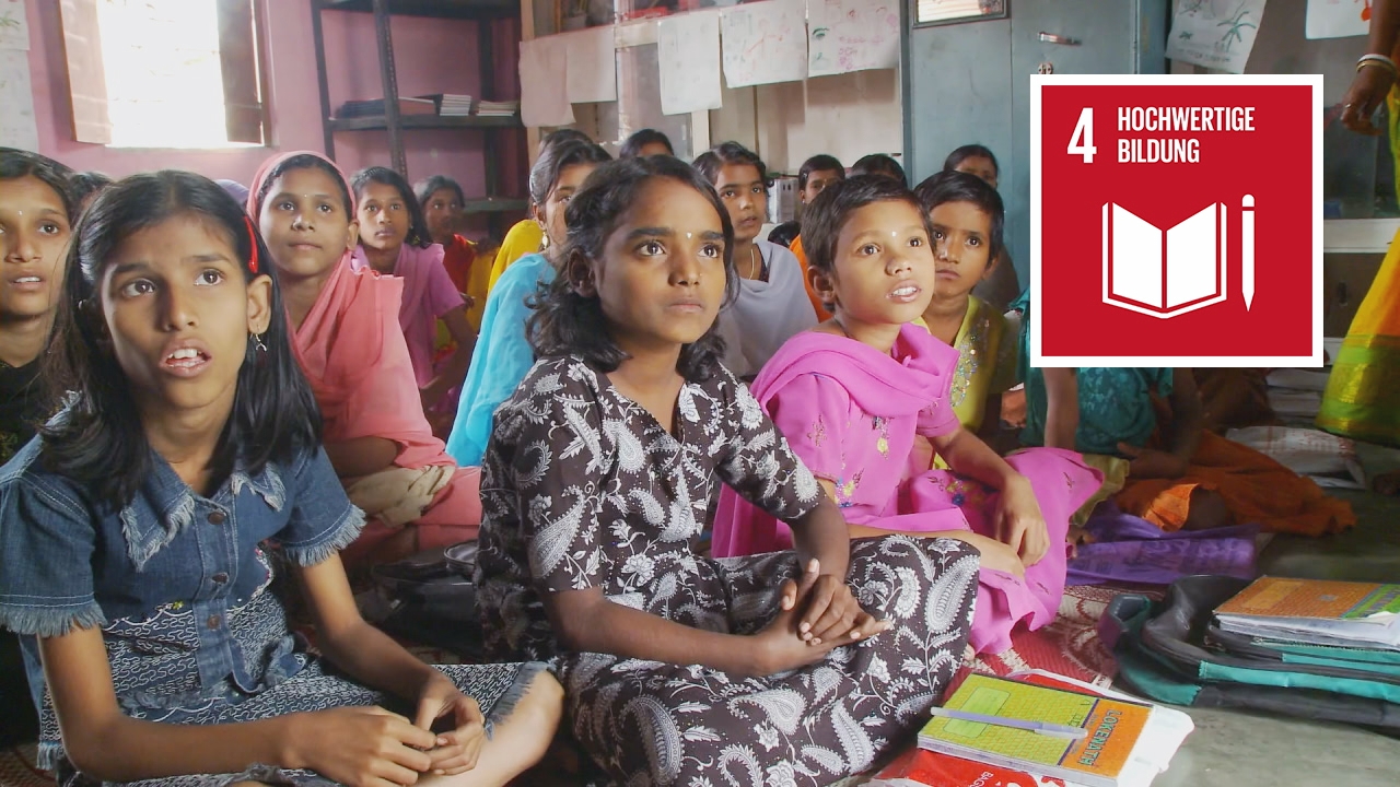 Gruppe von Mädchen in einem Klassenzimmer, die aufmerksam zuhören, mit Schulmaterialien vor ihnen.
