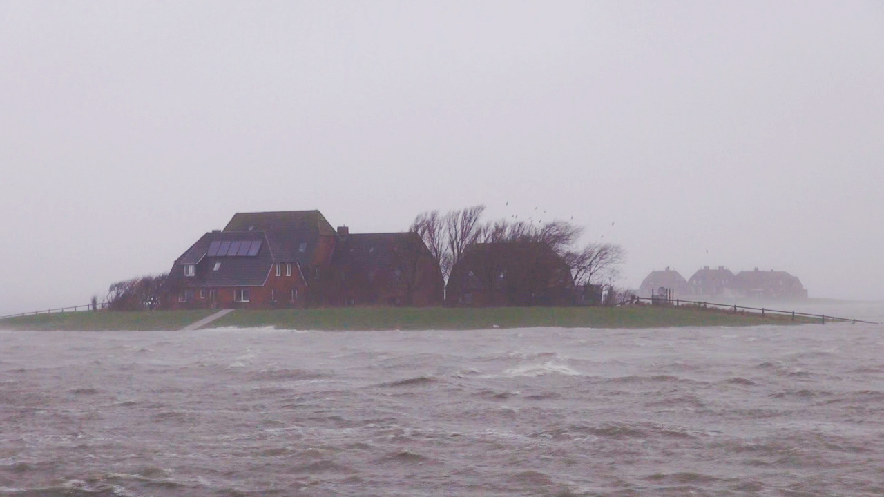 Eine kleine Insel mit einem roten Haus, umgeben von stürmischem Wasser und grauem Himmel.