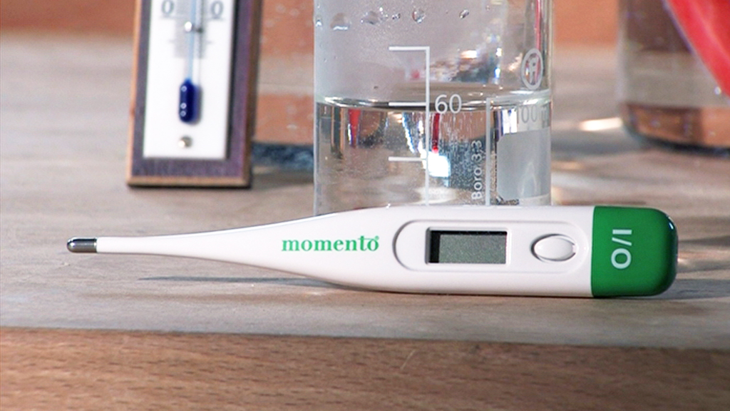 Digitales Thermometer mit grünem Kopf und LCD-Anzeige, neben einem Becher mit Wasser.