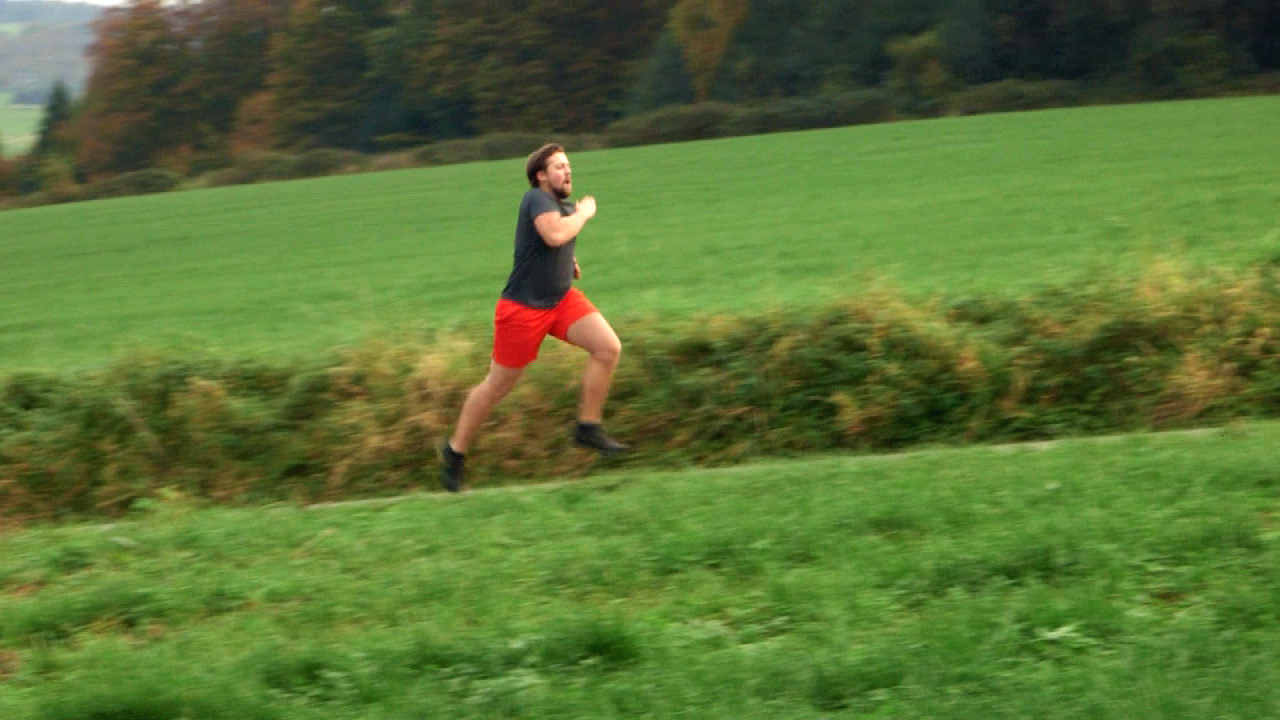 Eine Person in roter Shorts und schwarzem T-Shirt läuft über ein grünes Feld.