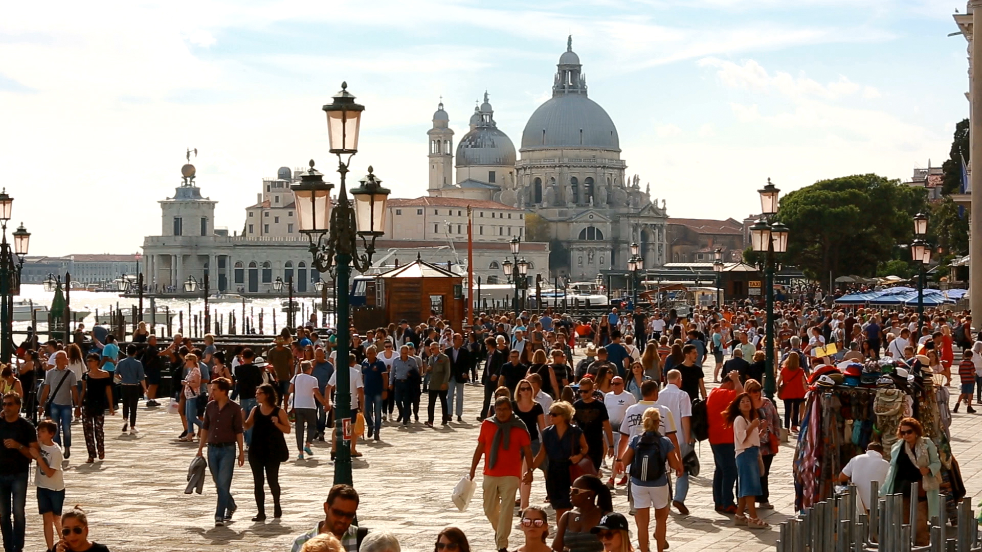 Menschenmenge auf einer Uferpromenade in Venedig mit der Basilica di Santa Maria della Salute im Hintergrund.