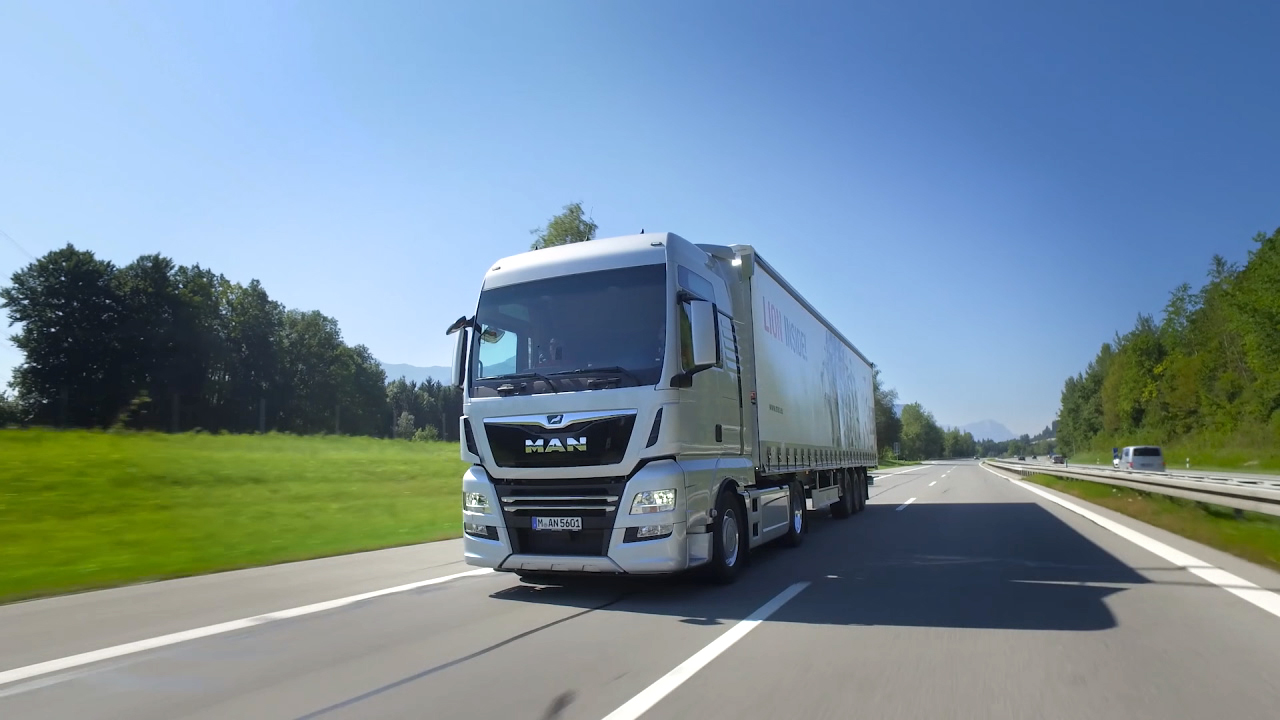 Ein MAN-Lkw fährt auf einer Autobahn, umgeben von grünen Wiesen und Bäumen.