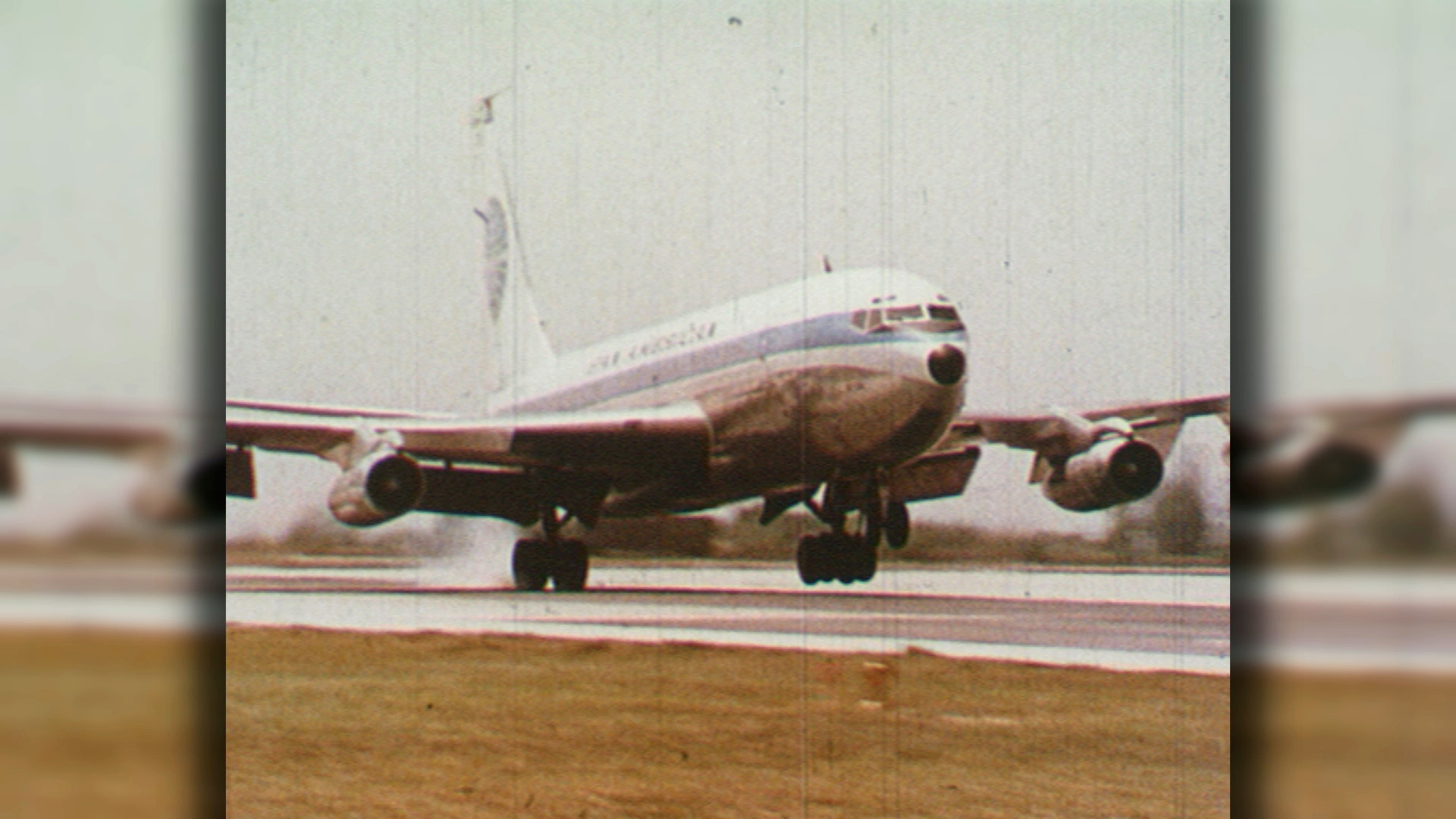 Ein Flugzeug landet auf einer nassen Landebahn, Wasser spritzt auf.