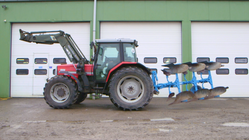 Roter Traktor mit einem blauen Pflug, der auf einem Feld steht.