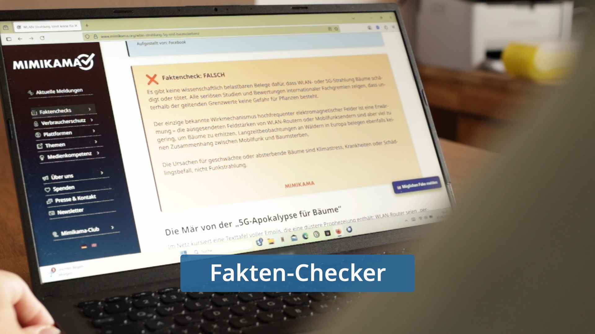 Laptopbildschirm zeigt Webseite von Mimikama mit Artikel über '5G-Apokalypse für Bäume' und hervorgehobenen Textabschnitt 'Faktencheck: FALSCH'.