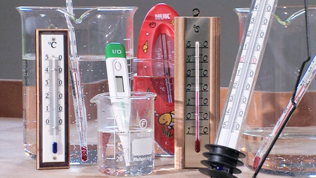 Verschiedene Thermometer und ein digitales Messgerät in Wasserbehältern, zur Temperaturmessung.