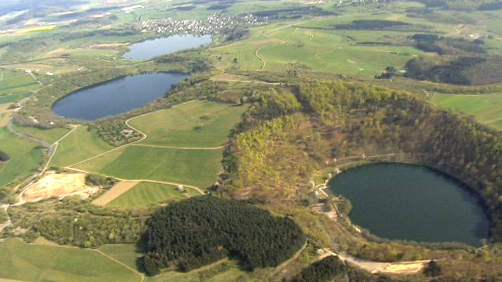 Luftaufnahme von zwei Kraterseen umgeben von grünen Feldern und Wäldern.