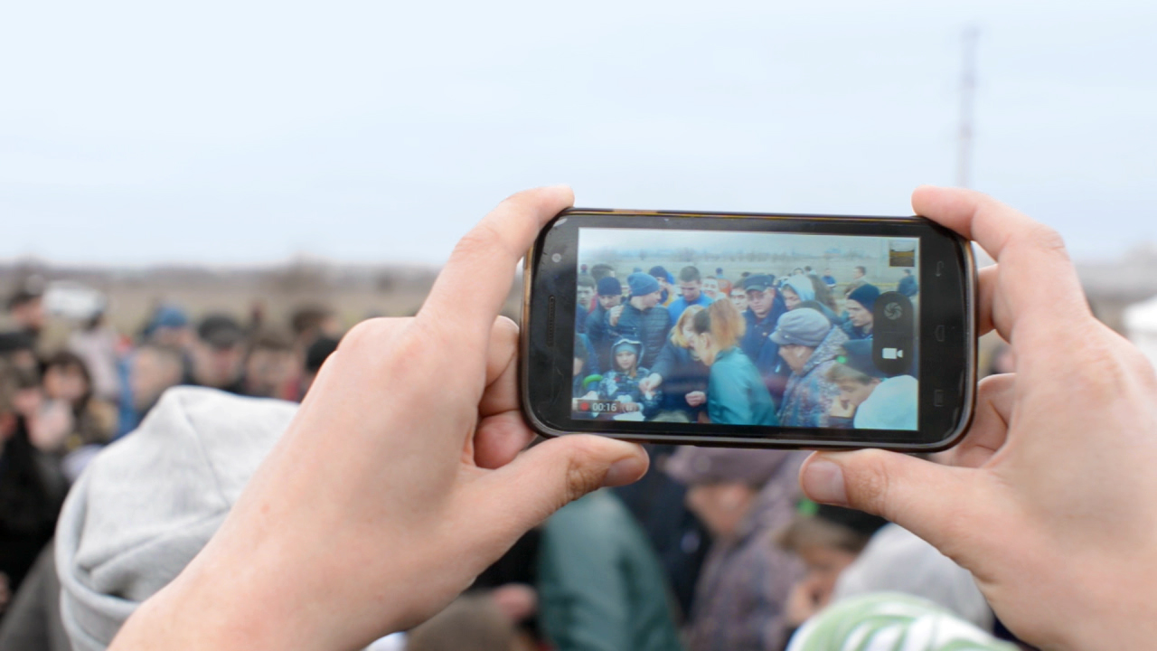 Eine Person hält ein Smartphone, um eine Menschenmenge zu fotografieren.