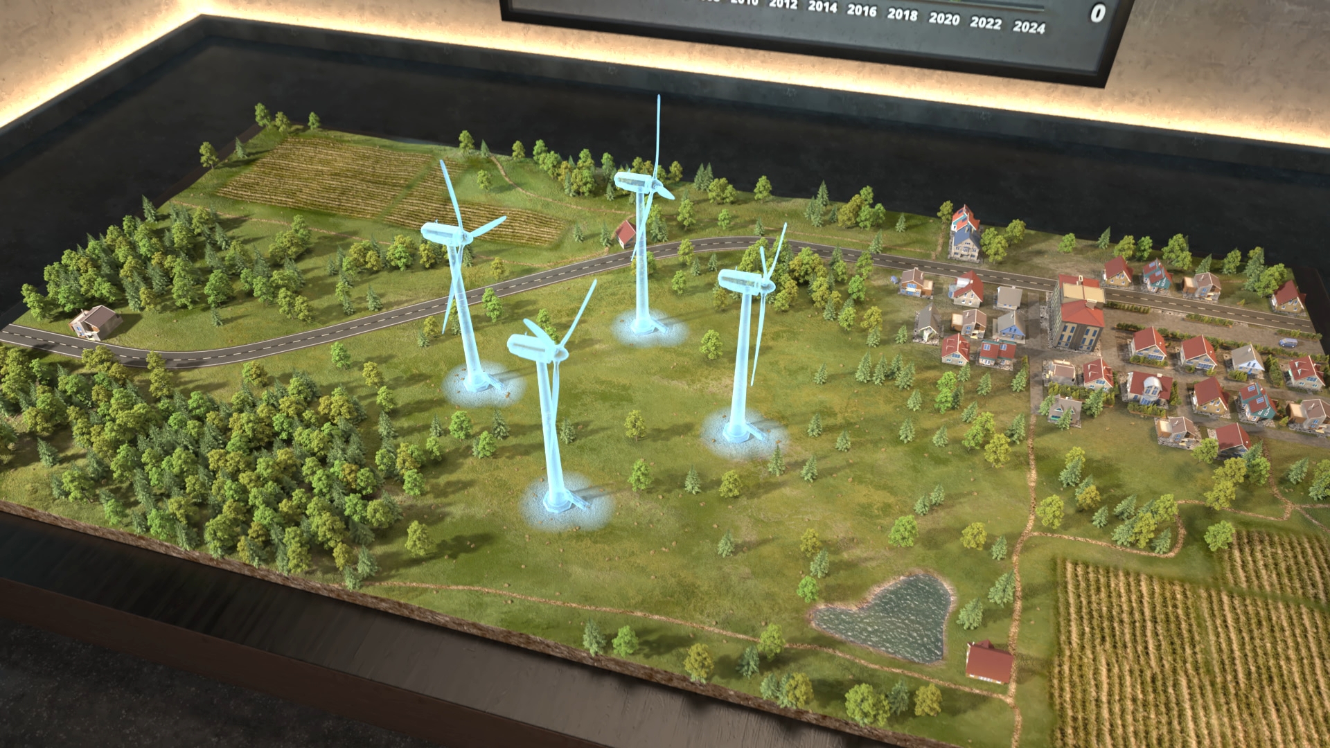 Modelllandschaft mit Windrädern auf grüner Wiese, umgeben von Wald, Feldern und einem kleinen Dorf mit Häusern.