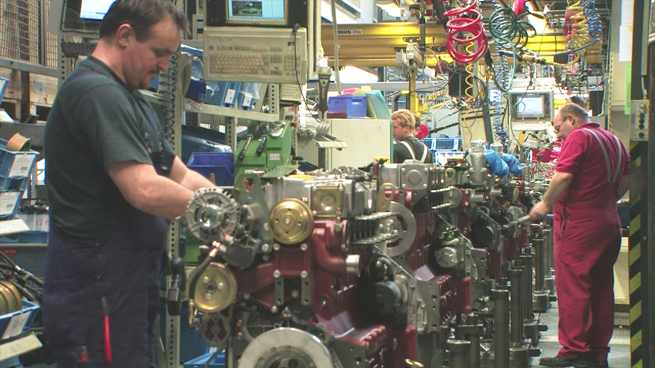 Arbeiter in einer Fabrik montieren Motoren an einer Produktionslinie.