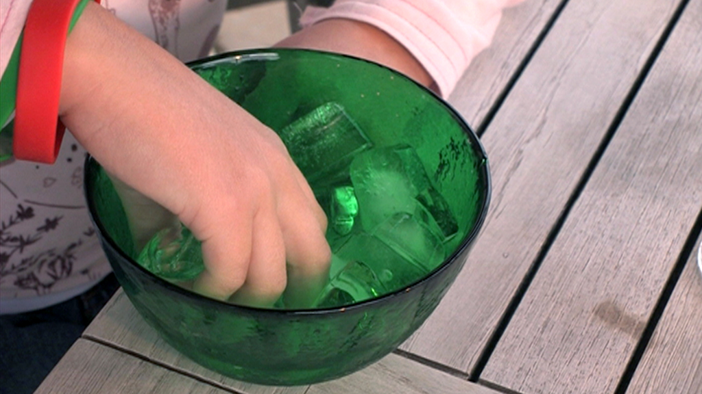 Eine Hand greift in eine grüne Schüssel mit Eiswürfeln.