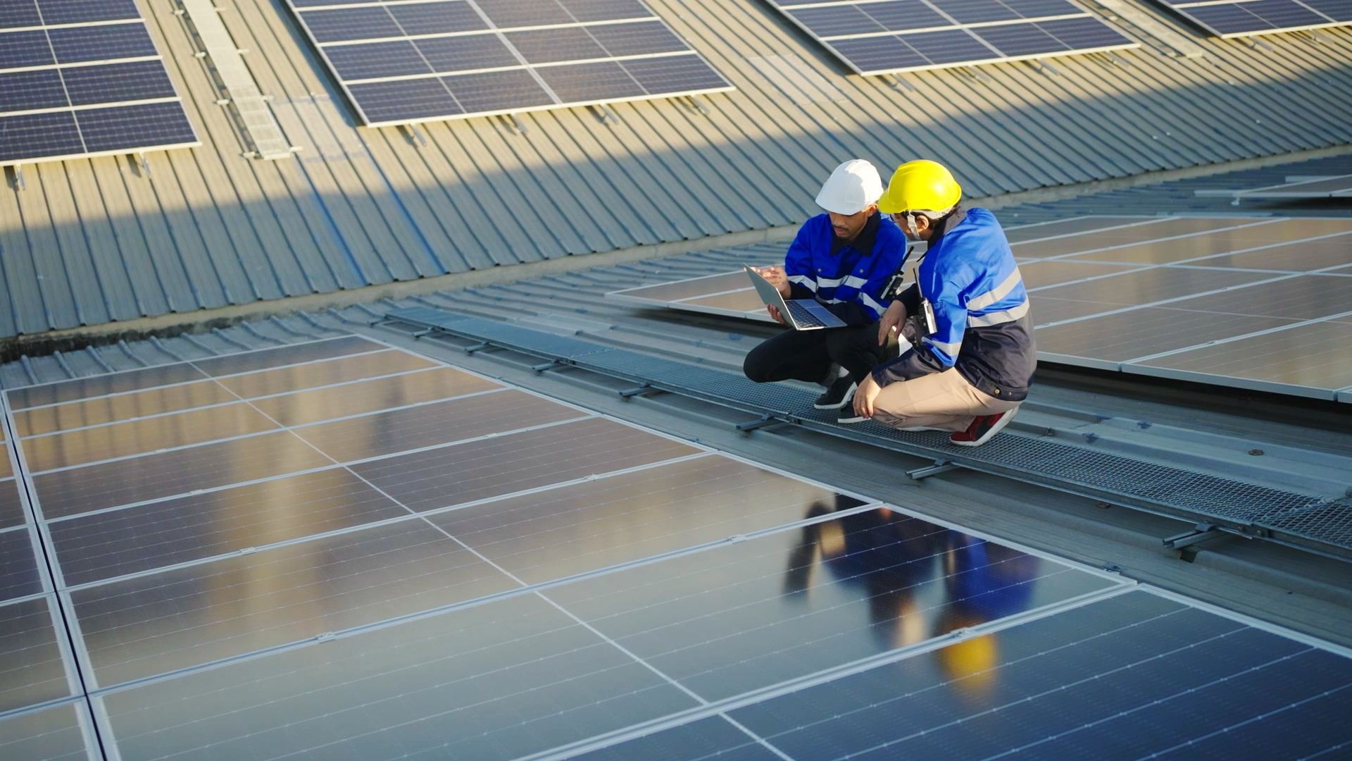 Zwei Techniker auf einem Dach mit Solarpanelen, einer überprüft die Daten auf einem Laptop, der andere beobachtet.