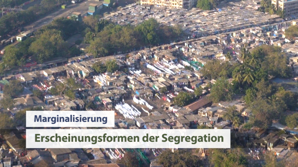 Luftaufnahme eines Slumgebiets mit dicht beieinander stehenden Hütten und Bäumen im Hintergrund.