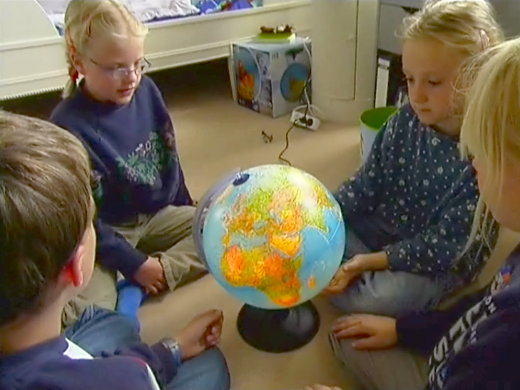 Vier Kinder sitzen im Kreis um einen Globus und betrachten ihn aufmerksam.