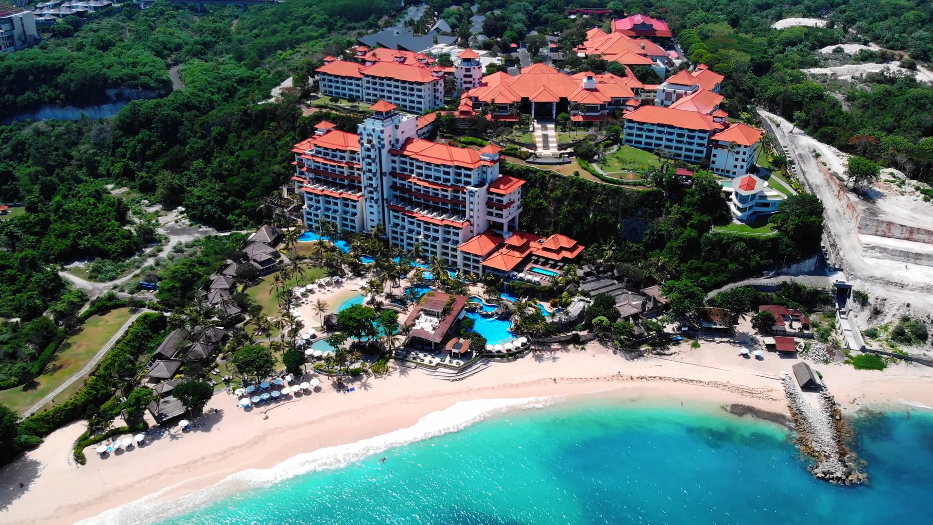Luftaufnahme eines Resorts an einem Strand mit türkisfarbenem Wasser und grüner Umgebung.