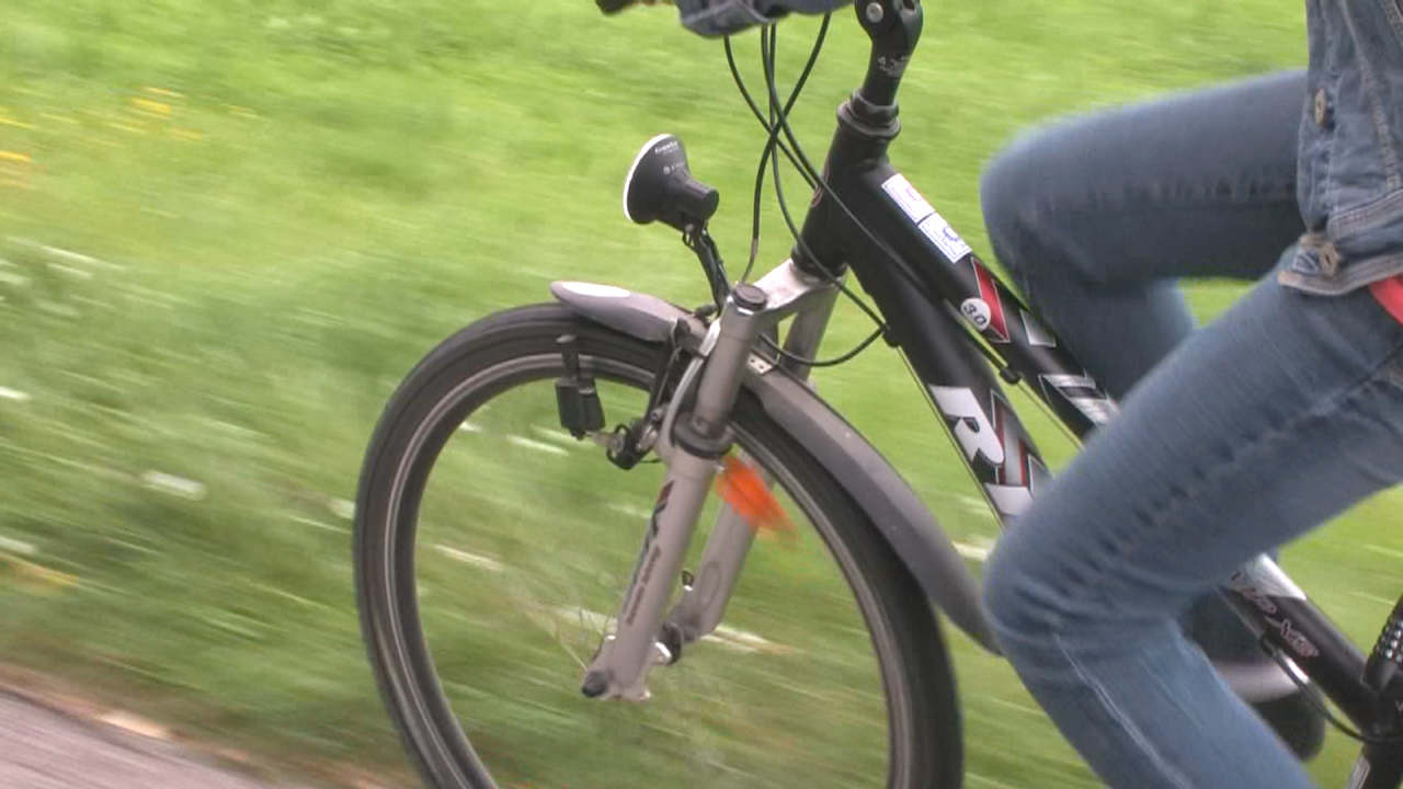Eine Person fährt auf einem schwarzen Fahrrad mit einem blauen Rahmen und Jeanshosen.