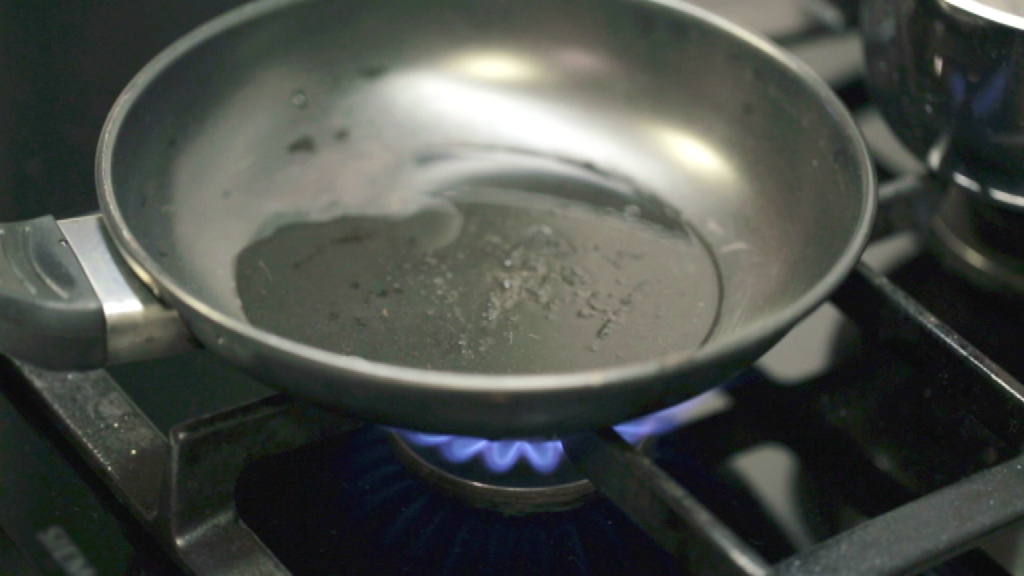 Eine Pfanne mit etwas Öl auf einem Gasherd, die auf einer blauen Flamme steht.
