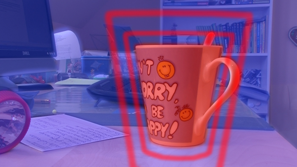 Eine orangefarbene Tasse mit dem Aufdruck 'Don't worry, be happy!' steht auf einem Schreibtisch.