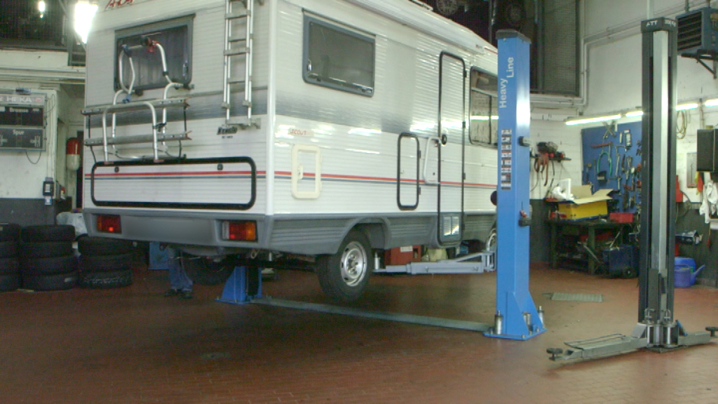 Ein Wohnmobil wird in einer Werkstatt auf einer Hebebühne angehoben.