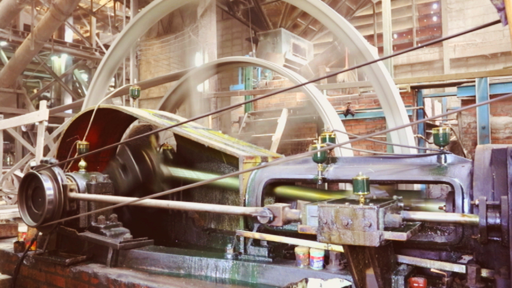 Dampfmaschine in einer historischen Fabrik, mit sichtbaren Zahnrädern und Rohren.