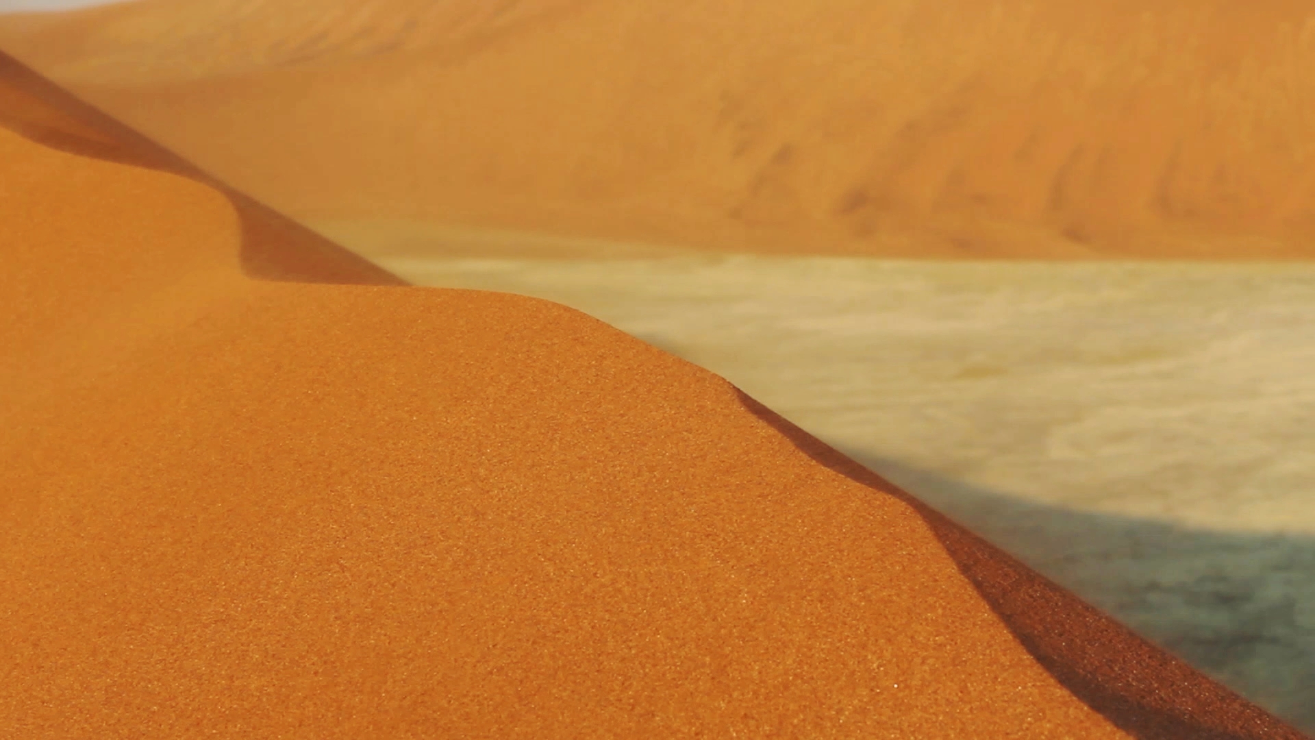 Nahaufnahme einer Sanddüne mit feinem, orangefarbenem Sand und einem hellen, unscharfen Hintergrund.