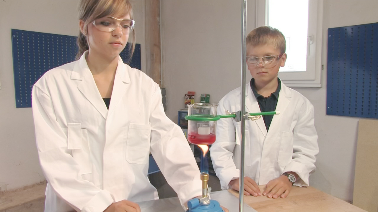 Zwei Schüler im Labor, einer führt ein Experiment mit einer Apparatur durch, der andere beobachtet.