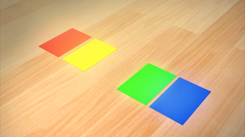 Vier farbige Quadrate (rot, gelb, grün, blau) auf einem Holzboden angeordnet.