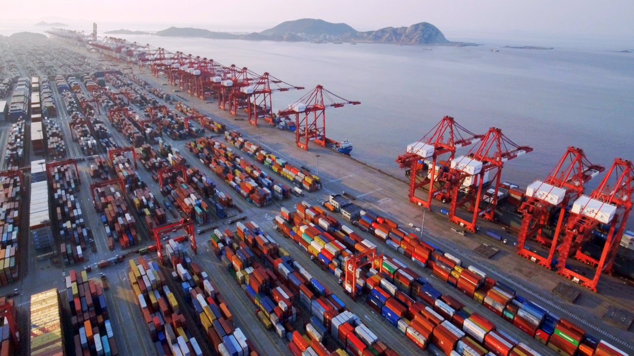 Luftaufnahme eines Containerhafens mit zahlreichen Containerschiffen und Kränen.
