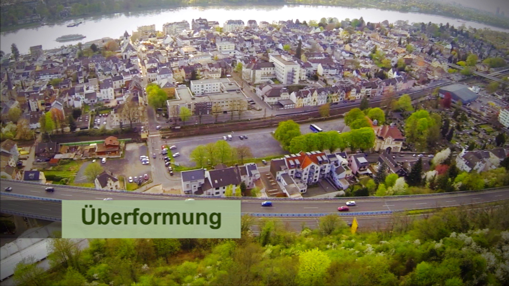 Luftaufnahme einer Stadt mit Wohngebieten, Straßen und Bäumen, beschriftet mit 'Überformung'.