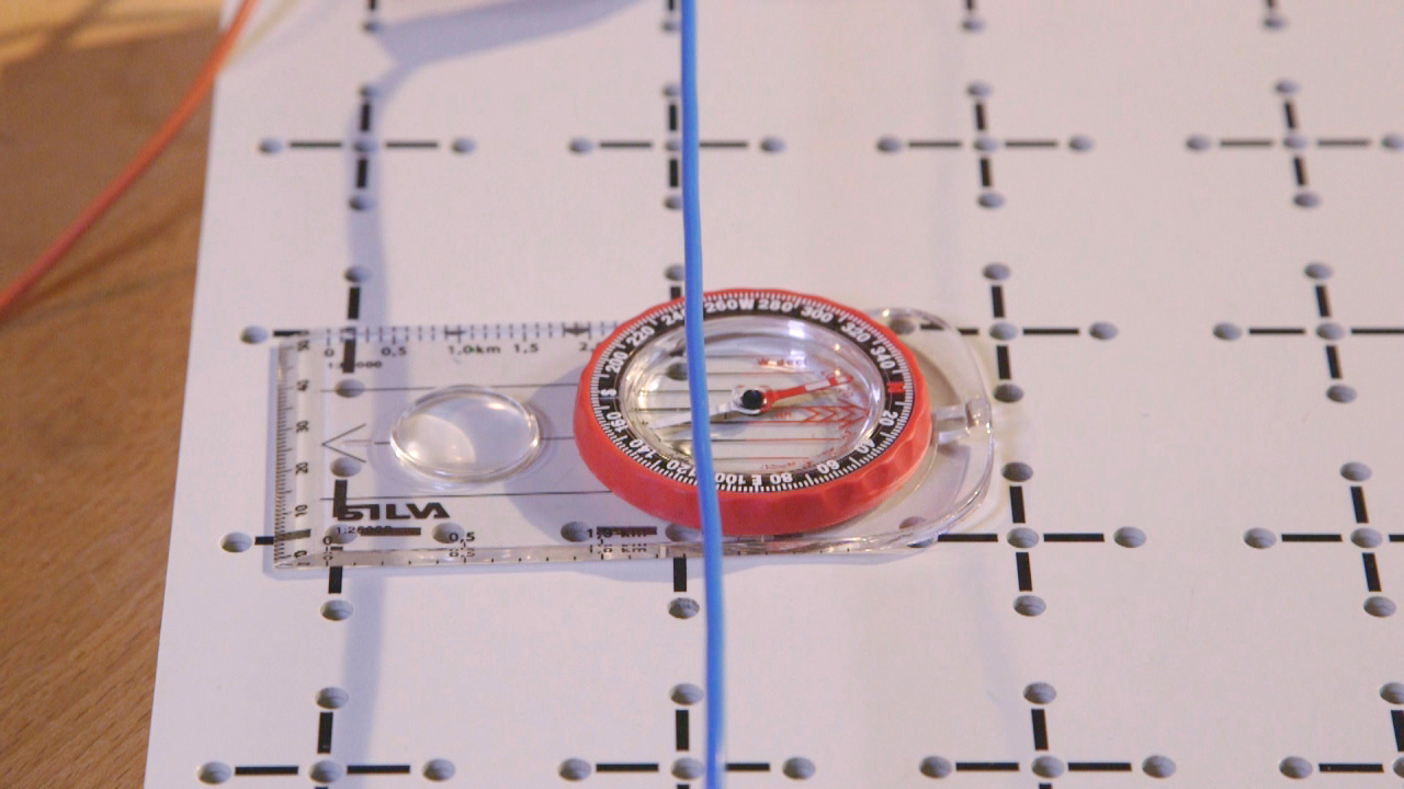 Ein Kompass auf einem weißen Blatt mit einem Rastermuster, daneben ein blauer Draht.