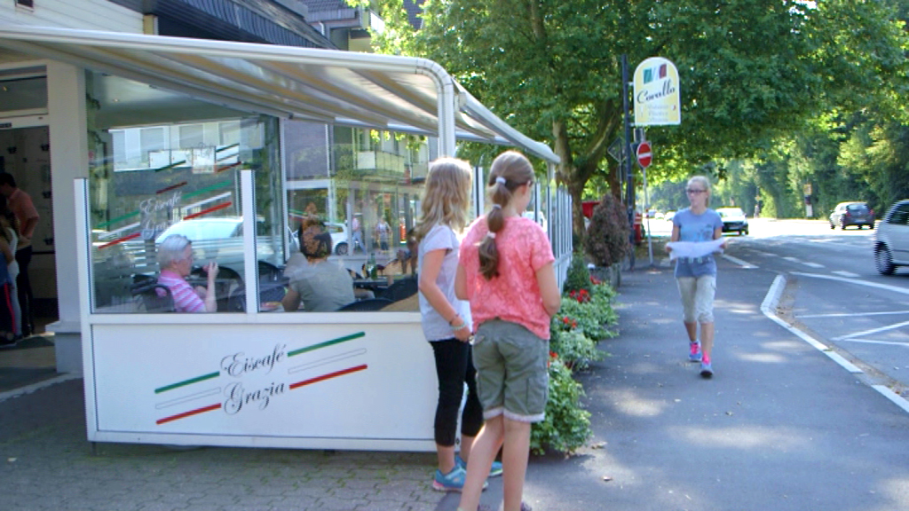 Zwei Mädchen stehen vor einem italienischen Restaurant mit Außenbereich, während eine Frau joggt.