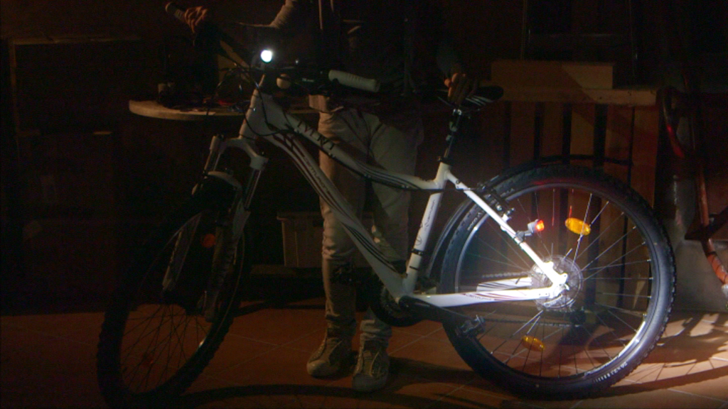 Ein Fahrrad mit eingeschaltetem Scheinwerfer steht neben einer Person in dunkler Umgebung.