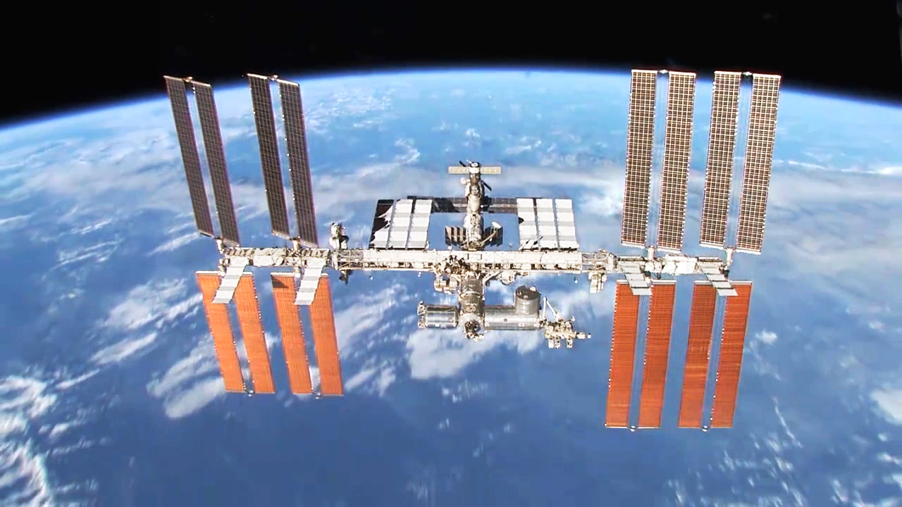 Die Internationale Raumstation (ISS) schwebt über der Erde, umgeben von Wolken und dem Weltraum.