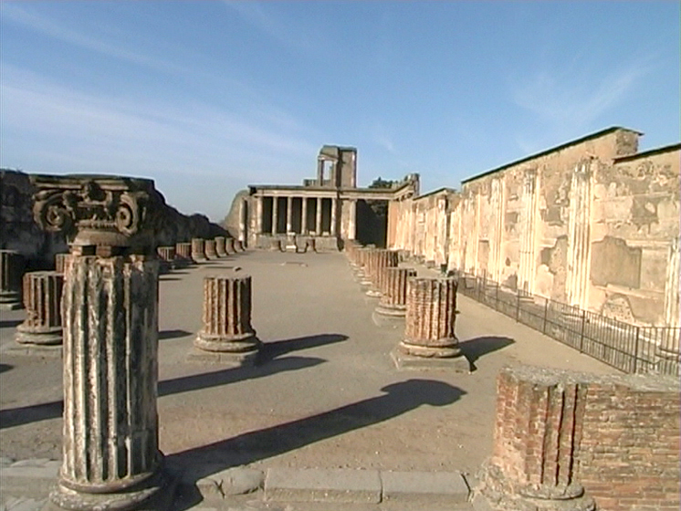 Ruinen von Pompeji mit Säulen und Gebäuden im Hintergrund unter blauem Himmel.