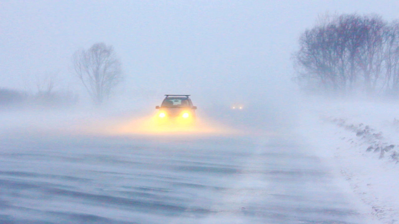 Ein Auto fährt durch starken Schneefall und Sichtbehinderung auf einer verschneiten Straße.
