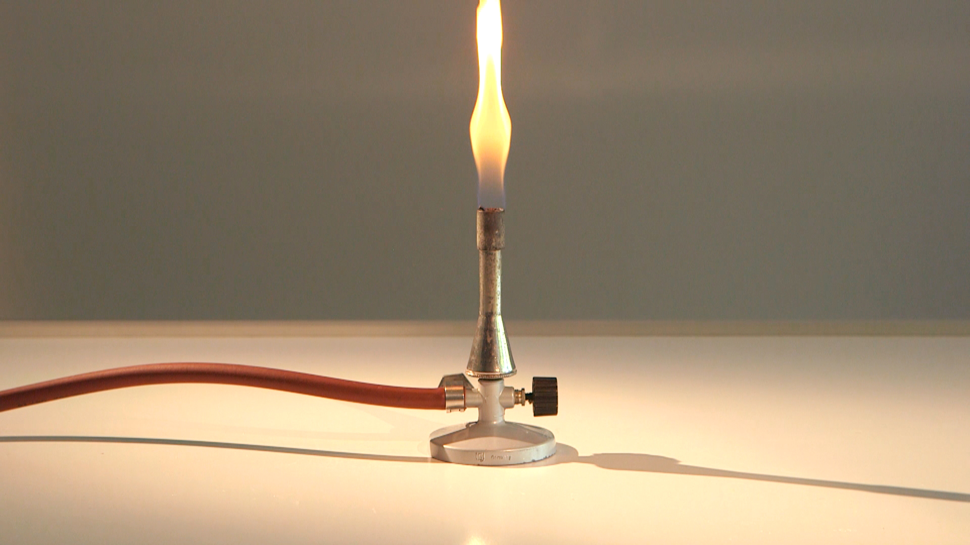 Ein Bunsenbrenner mit einer Flamme, die aus der Düse aufsteigt, auf einem Tisch.