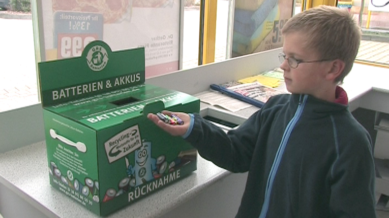 Ein Junge gibt Batterien in eine grüne Sammelbox für Batterien und Akkus.
