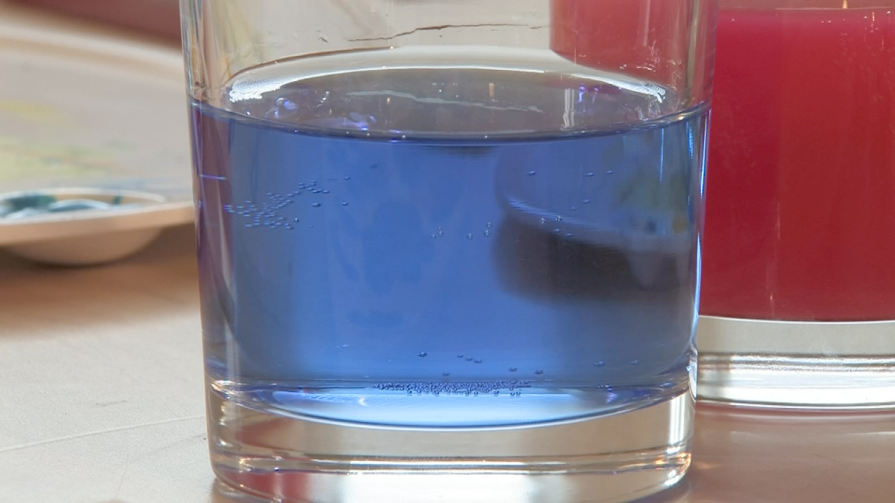 Ein Glas mit blauer Flüssigkeit, im Hintergrund ein rotes Glas.