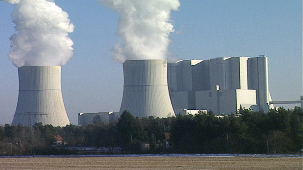 Kernkraftwerk mit zwei Kühltürmen, die Dampf ausstoßen, umgeben von Bäumen und einem klaren Himmel.