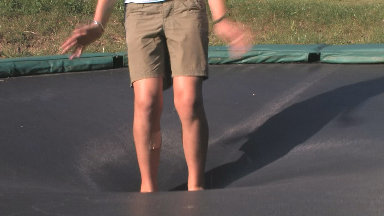 Ein Kind springt auf einem Trampolin, das in der Mitte nach unten gewölbt ist.