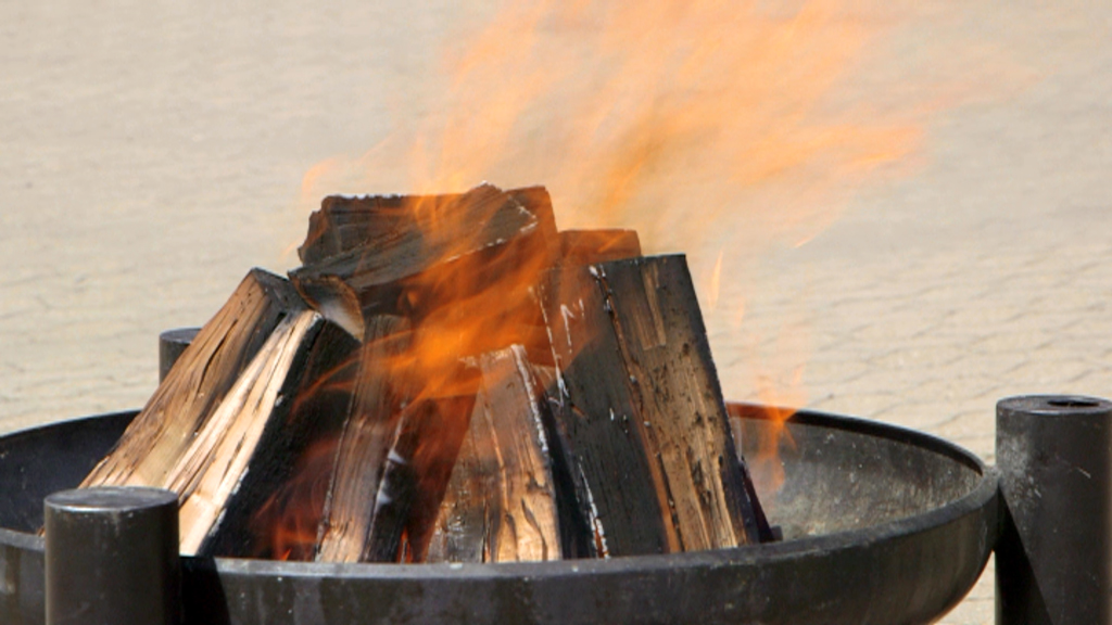 Ein Lagerfeuer mit brennendem Holz in einem runden Feuerkorb.