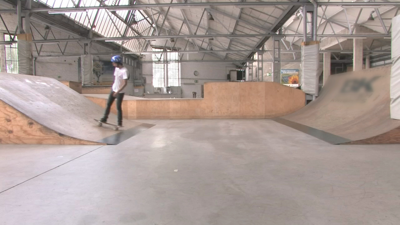 Skateboardfahrer in einer Skatehalle, der auf einer Rampe fährt.