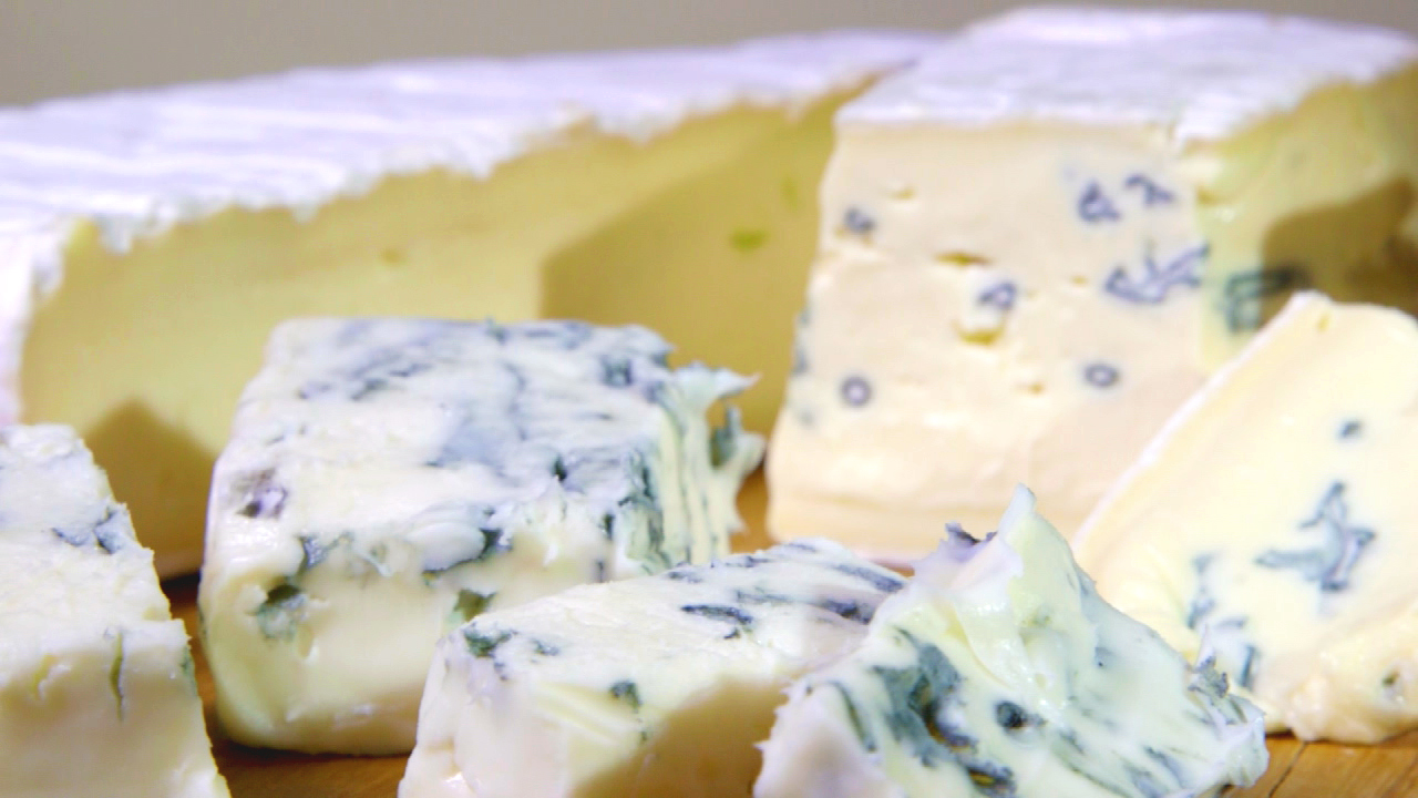 Verschiedene Stücke von Blauschimmelkäse auf einem Holzbrett, mit einer cremigen Textur und blauen Adern.