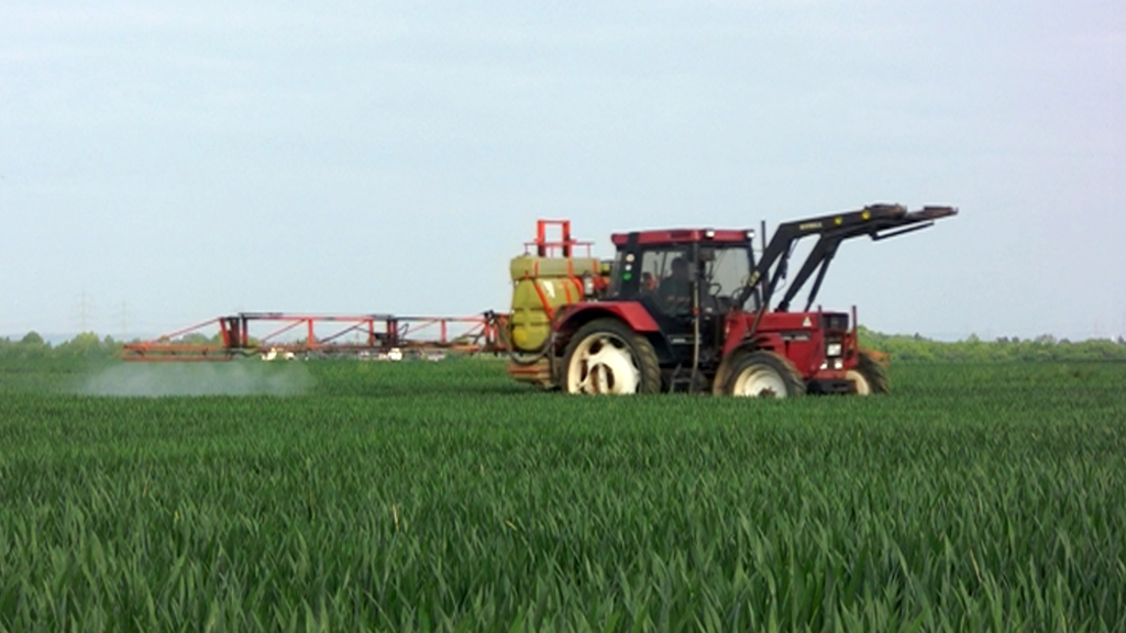 Ein roter Traktor sprüht Pestizide auf ein grünes Feld.