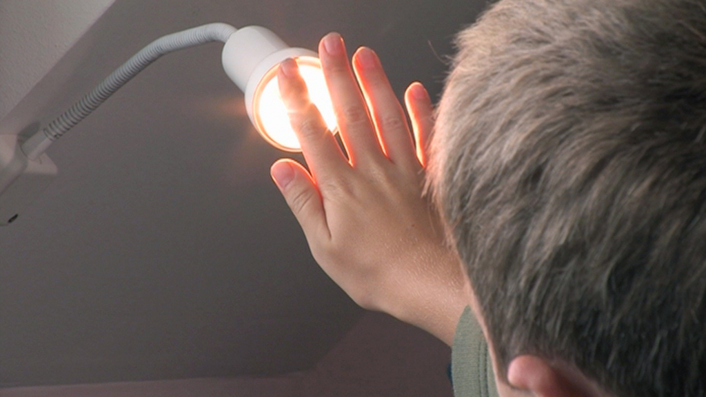 Eine Person hält die Hand nahe an eine leuchtende Lampe, um das Licht zu spüren.