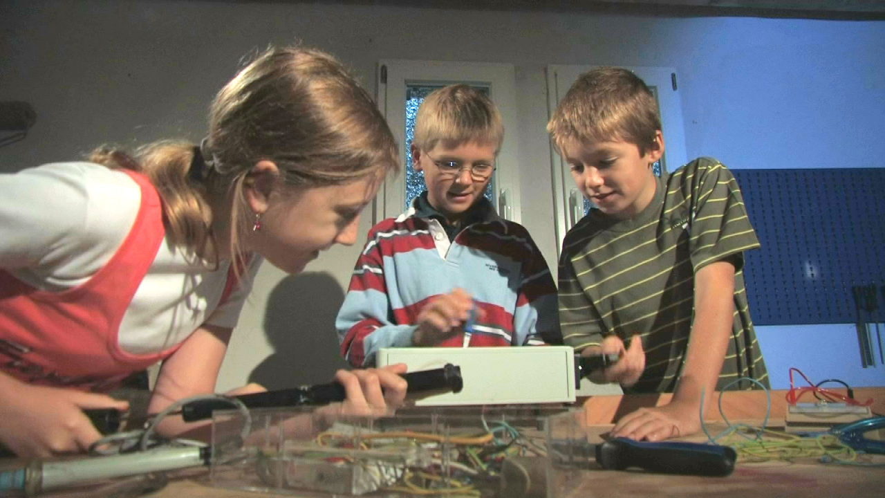 Drei Kinder arbeiten gemeinsam an einem Projekt, während sie Werkzeuge und Materialien verwenden.