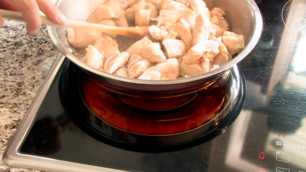Hähnchenstücke werden in einer Pfanne mit einem Holzlöffel gebraten.